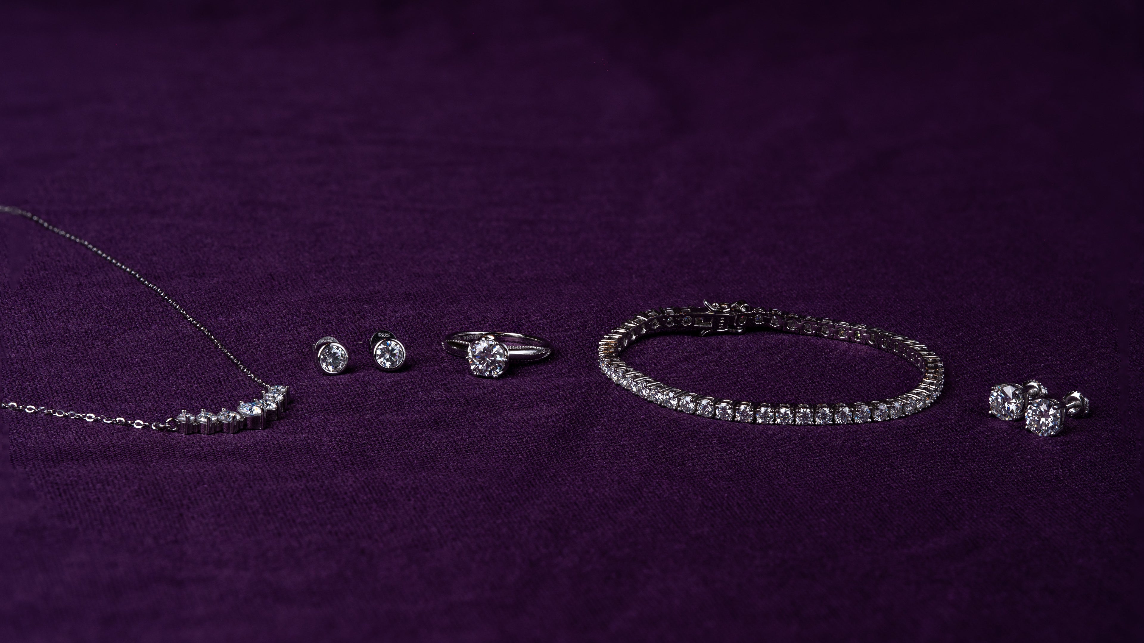 Veyelle moissanite jewelry collection featuring Borde ring, Éclat bracelet and Pura earrings on plum velvet background1621243260e1af0c20-0